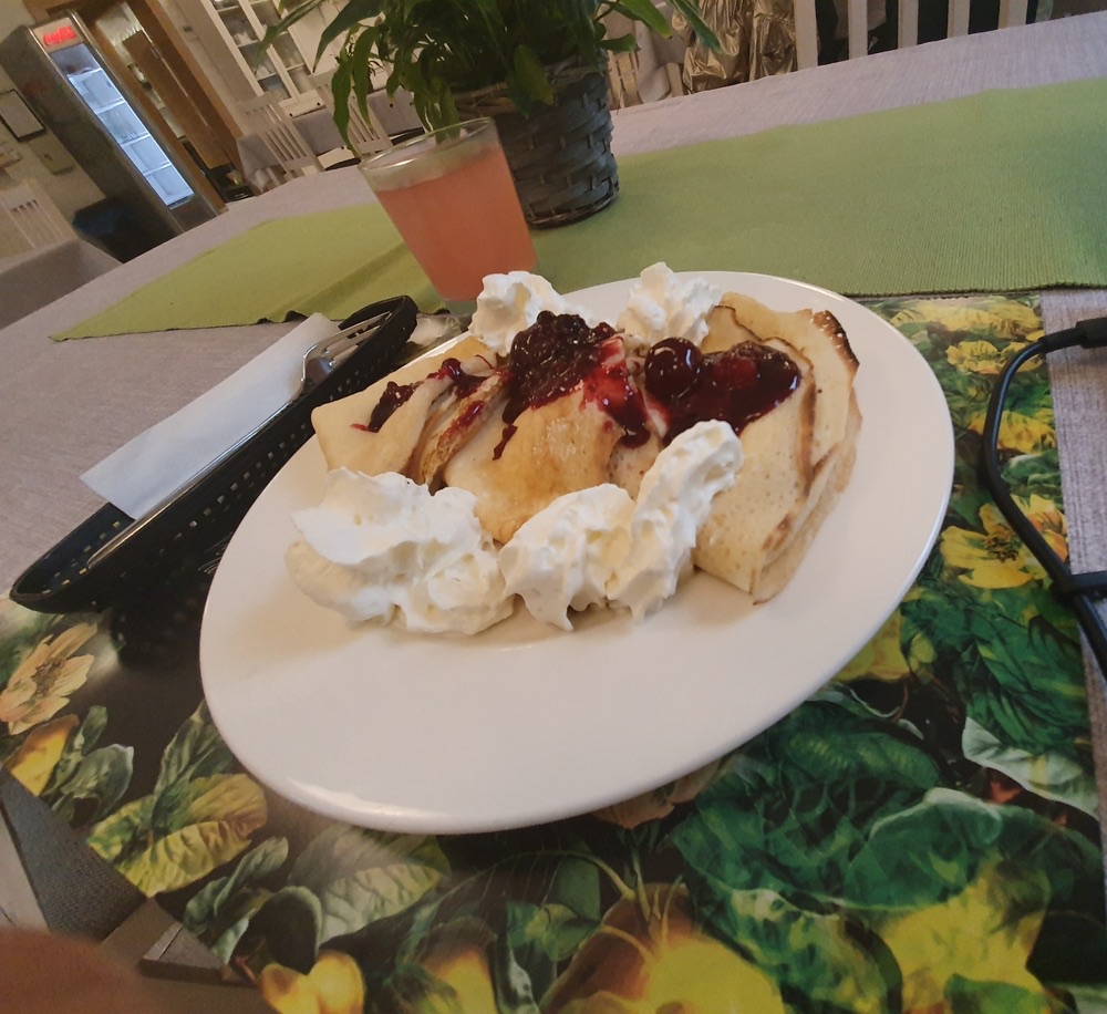 Naleśniki z bitą śmietaną i sosem jagodowym na białym talerzu